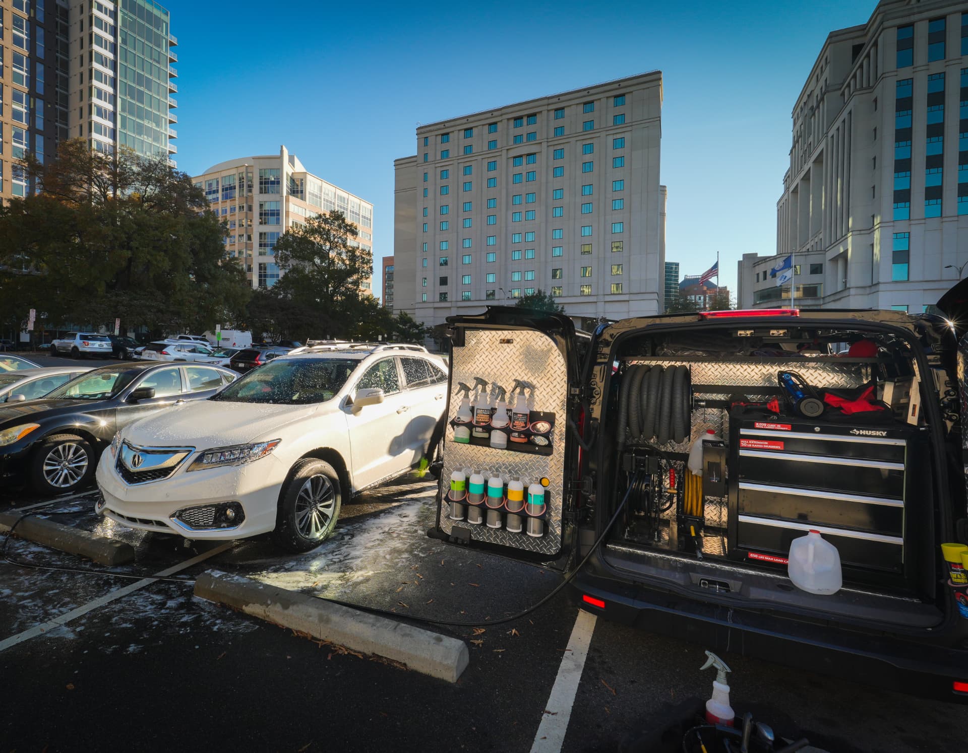 Tilicare detailer washing a soap-covered SUV beside the Tilicare mobile detailing van with its doors open