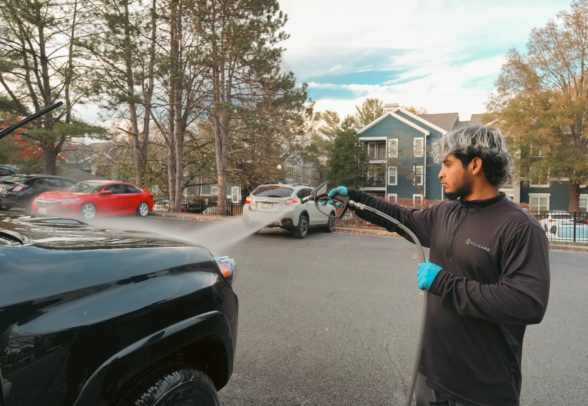 Tilicare detailer pressure washing a black car in a residential parking lot