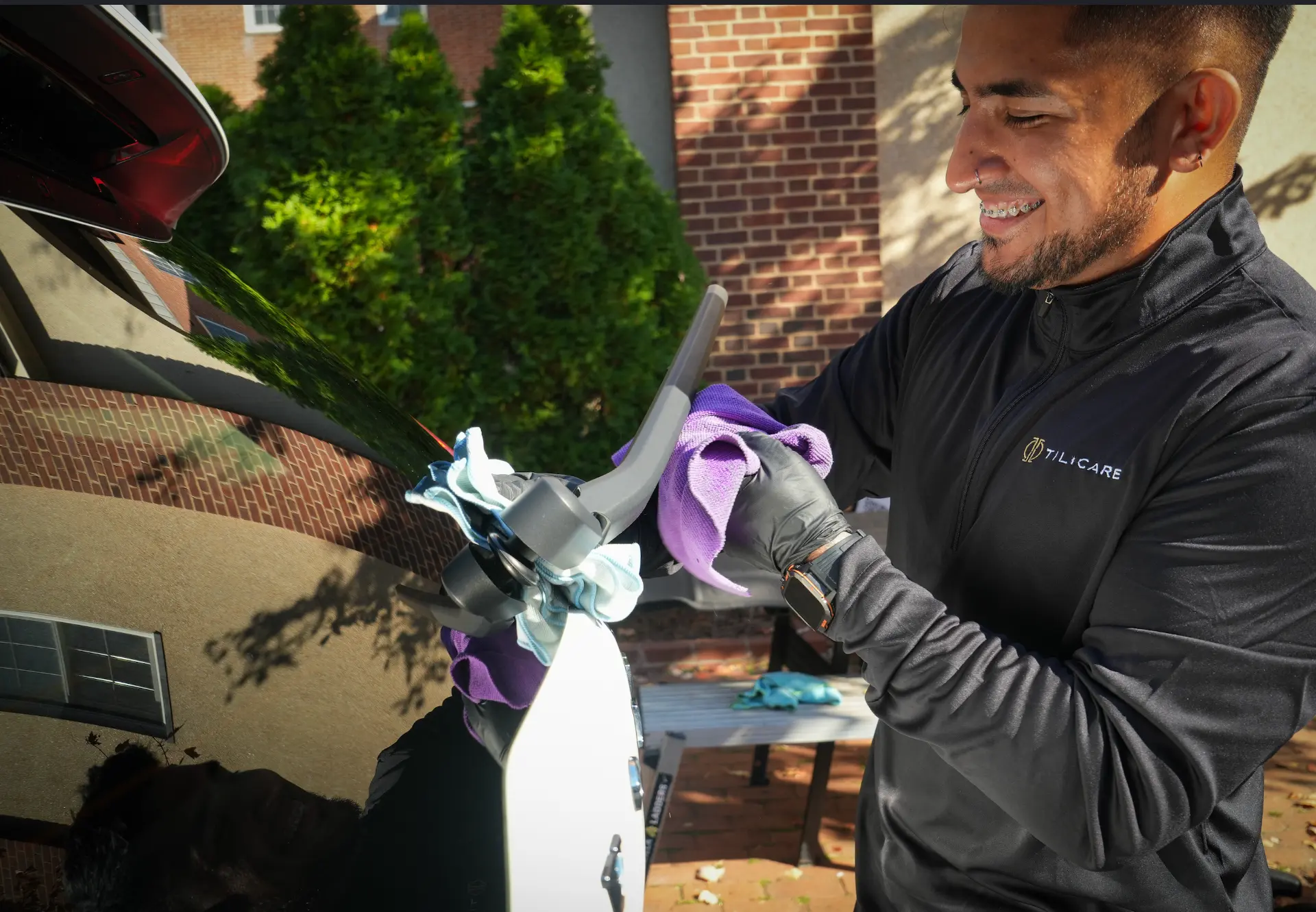Tilicare detailer in a branded shirt drying a car's rear window with microfiber cloths